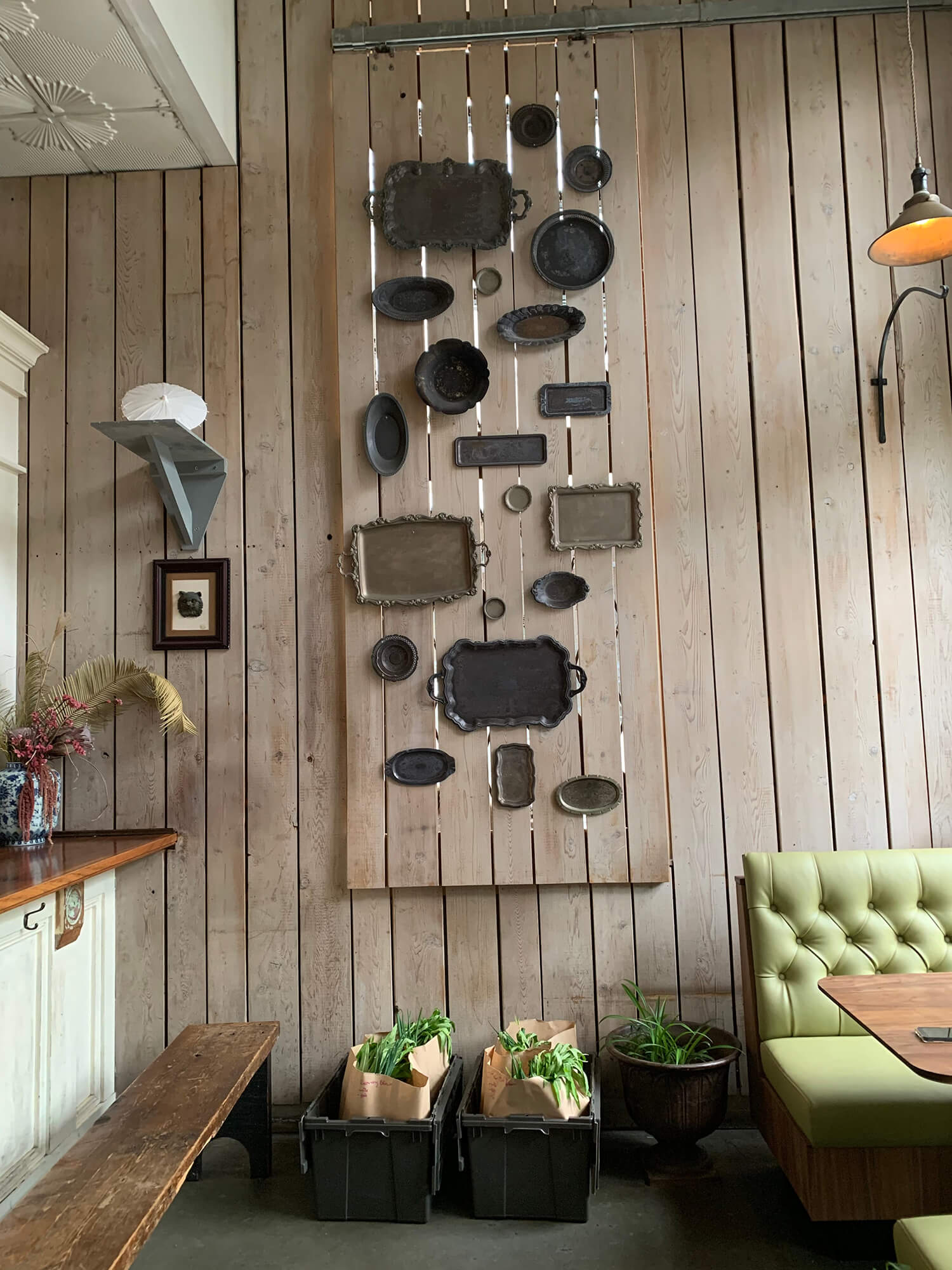Bao Bei restaurant interior. Rustic wood planks affixed vertically along the wall from floor to ceiling are decorated with tarnished antique silver trays. Bins of groceries in paper bags are placed against the wall.