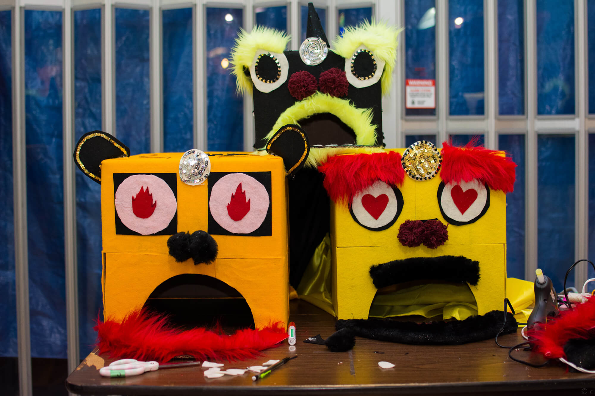 Three handmade arts and crafts lion dance heads made out of cardboard boxes with felt cut-outs for eyes and fake fur for trimming.
