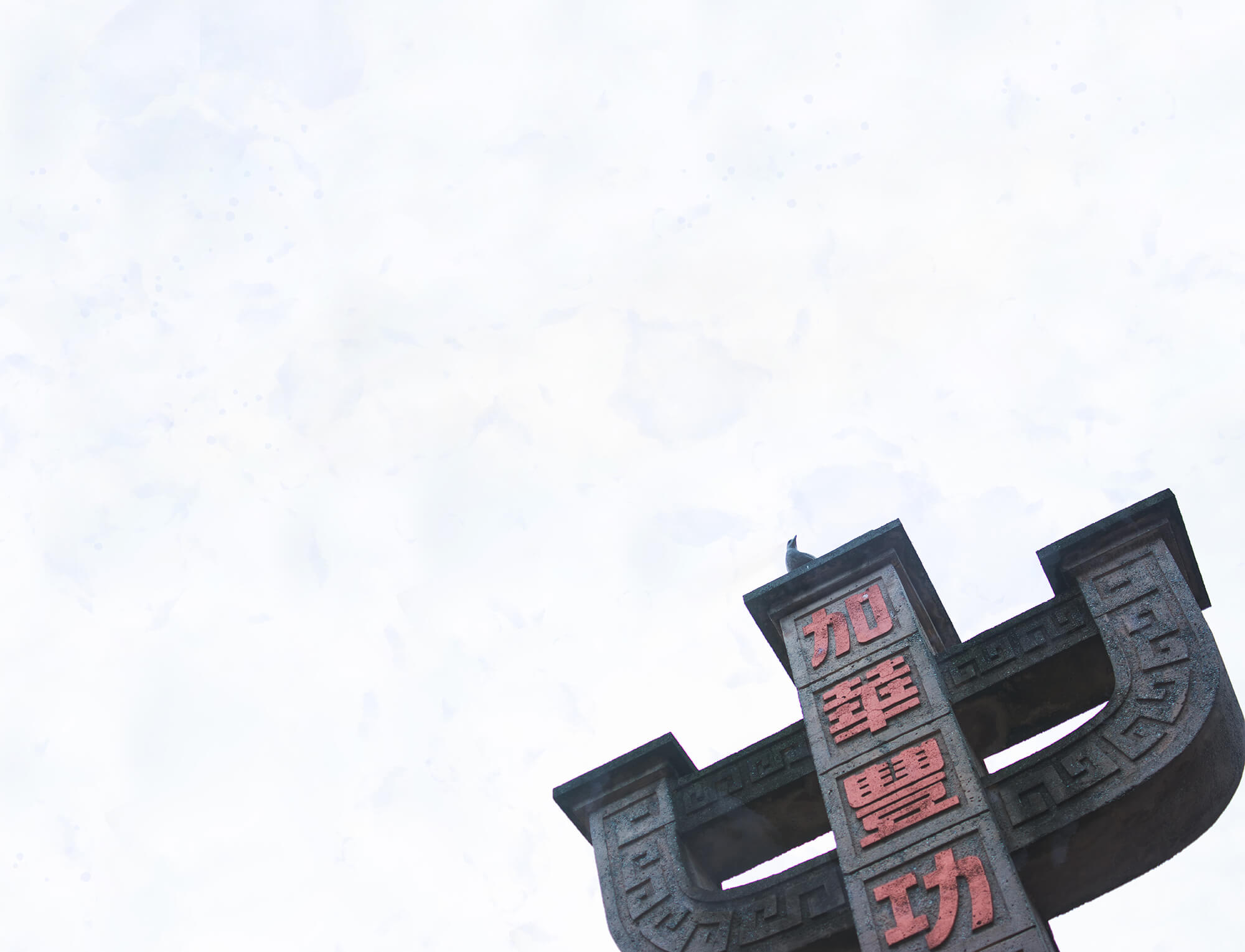 The Chinatown Memorial Monument in Chinatown Memorial Plaza, captured from below. A bird rests atop the monument against the backdrop of a faintly blue sky.